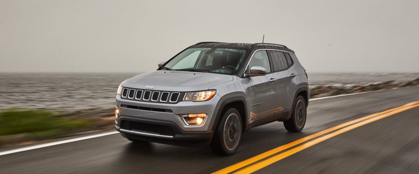 The 2020 Jeep Compass being driven on a rainy road by the lake.