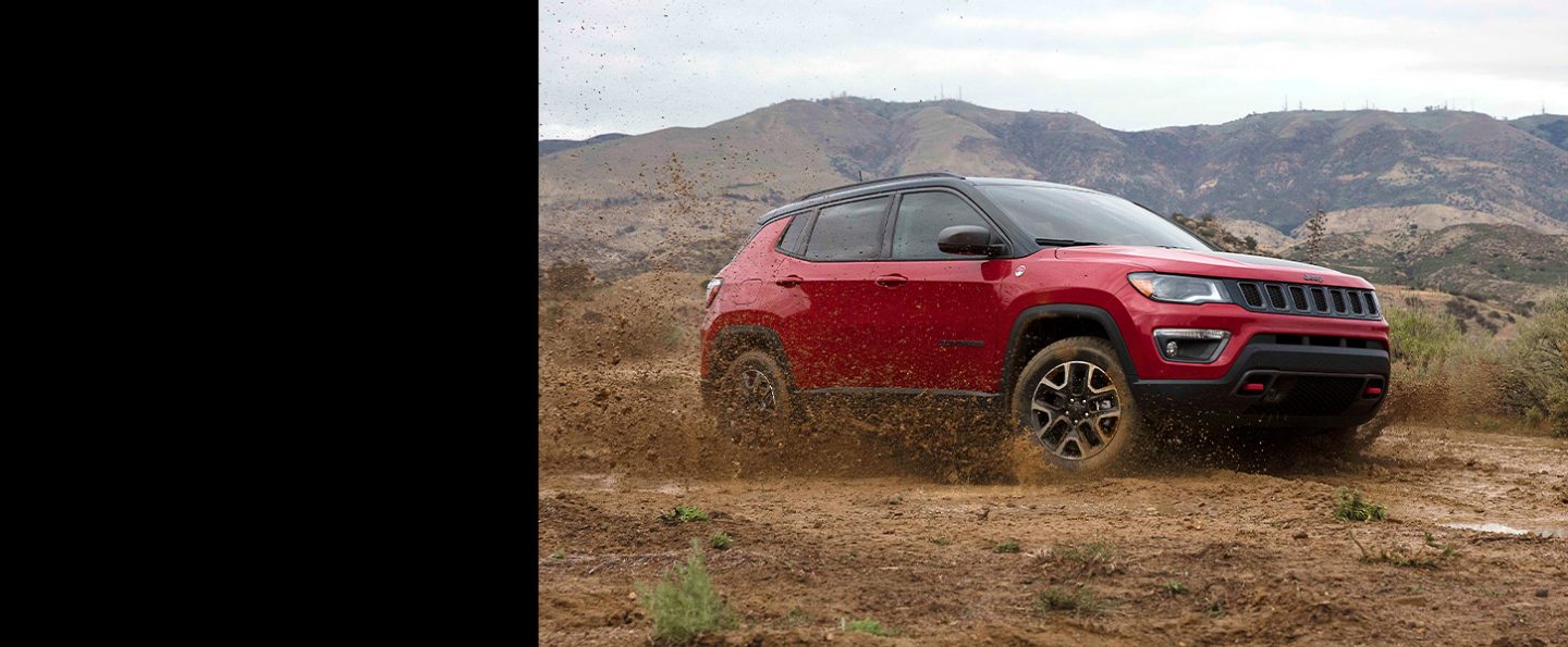 The 2021 Jeep Compass churning up mud from its wheels as it's driven off-road.