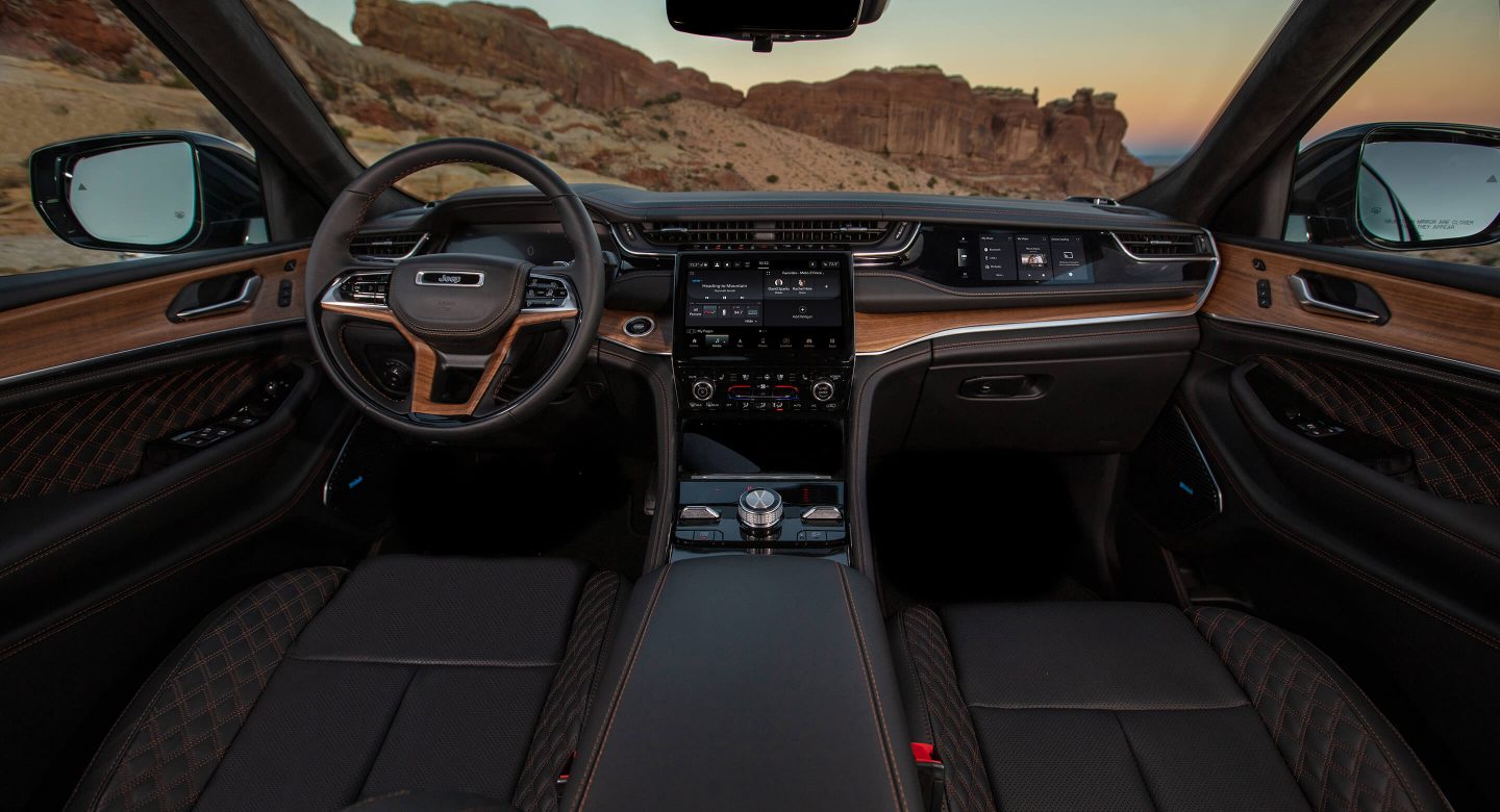 The front row of the 2022 Jeep Grand Cherokee Summit Reserve, in Tupelo Palermo leather, focusing on the steering wheel, touchscreen and dashboard.