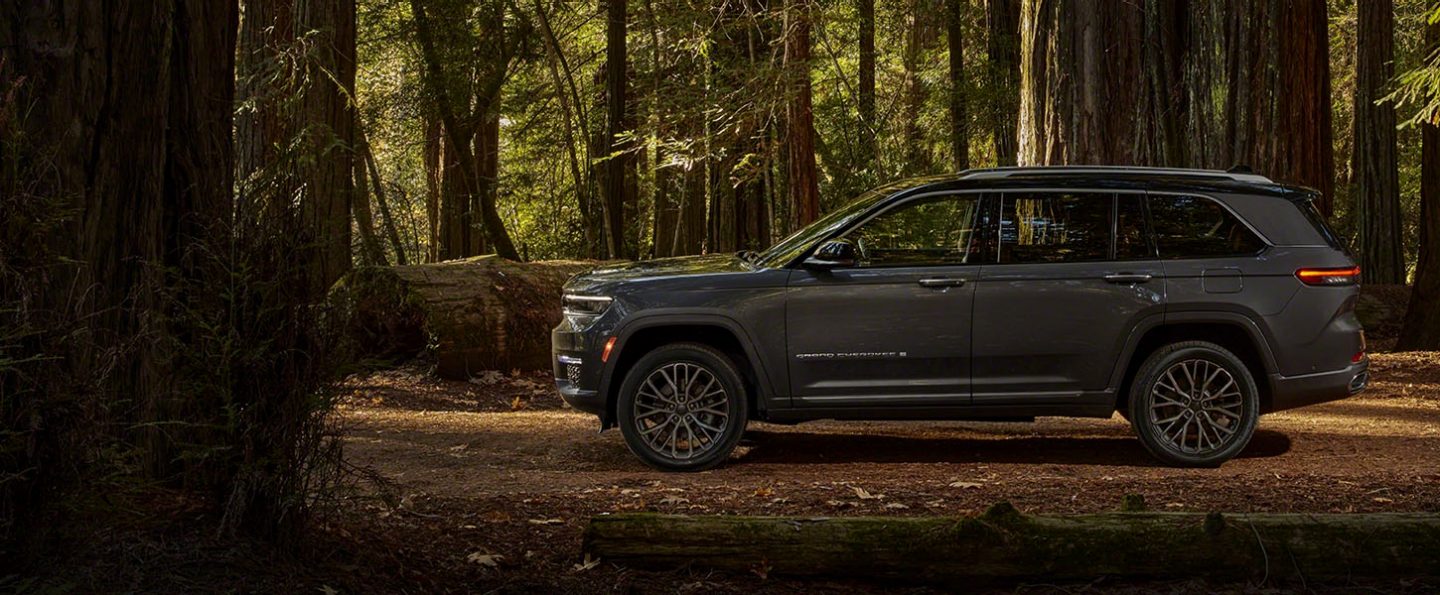 A side profile of the two-row 2022 Jeep Grand Cherokee L Summit Reserve against a backdrop of trees, allowing the viewer to estimate its length.