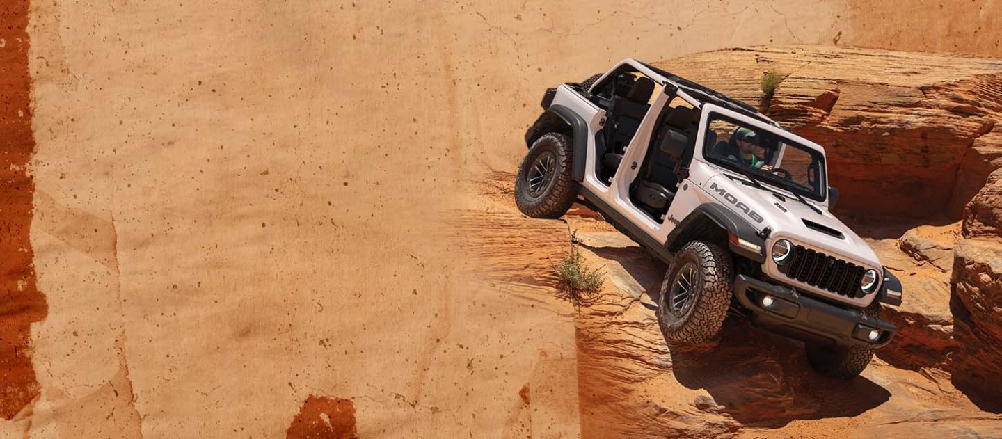A white 2026 Jeep Wrangler Moab 392 with its doors and top removed, descending a huge rock formation.